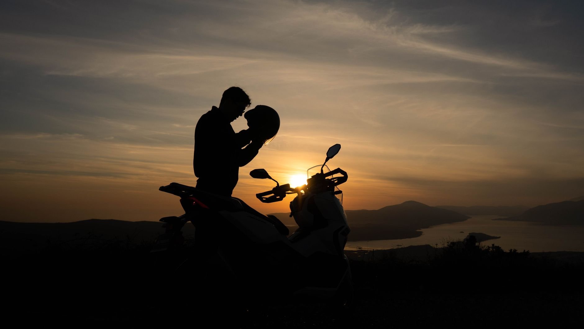 Silhouette of a biker preparing to ride a motorcycle against a stunning sunset backdrop.